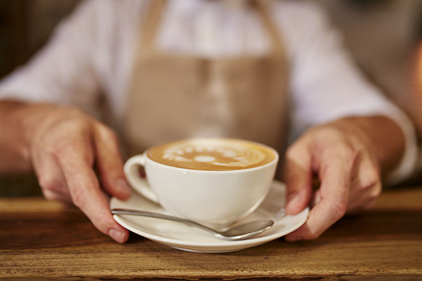 48554255 - close up of man serving coffee while standing in coffee shop. focus on male hands placing a cup of coffee on counter.