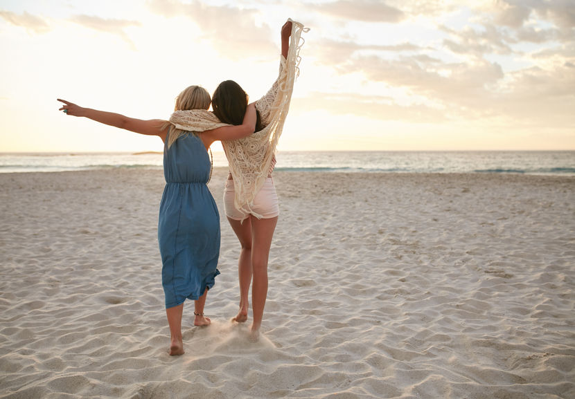 58801488 - full length rear view shot of two young women walking on the beach with their hands raised. female friends having fun on the sea shore.